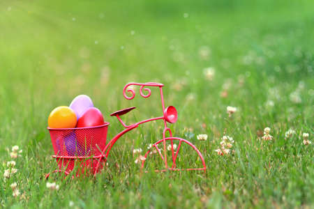 Colorful easter eggs in the basket of a pink tricycle in the grass.の写真素材