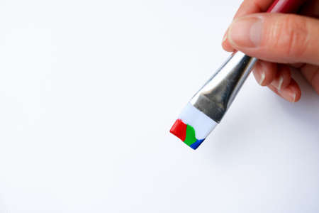 Woman's hand holding a paint brush dipped in red, green and blue paint