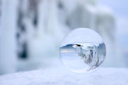 Transparent glass ball reflecting an ice covered bush beside a lakeの写真素材
