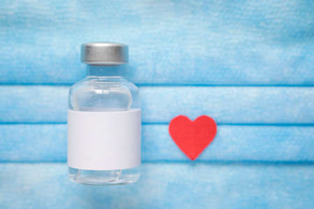 Red heart displayed with a vial of injectible medicine on a blue medical mask