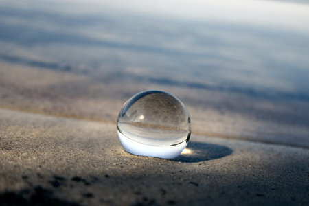 Glass lens ball on the beach reflecting the lake and skyの写真素材