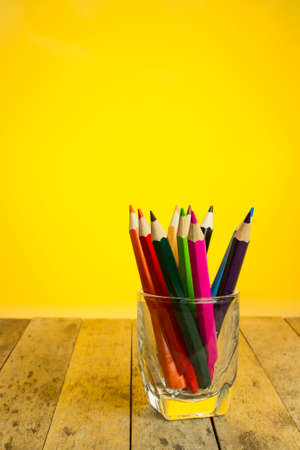 color pencils in a glass on wood plank, yellow backlight backgroundの写真素材