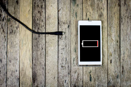 smart phone need to charge a battery on wood plank, top view