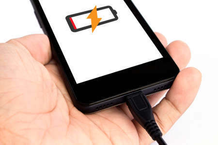 human's hand holding smart phone is charging on white backgroundの写真素材