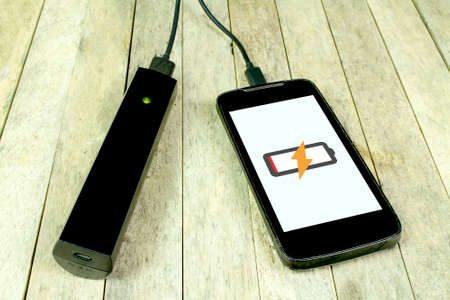 Smart phone is charging by power bank on wood background