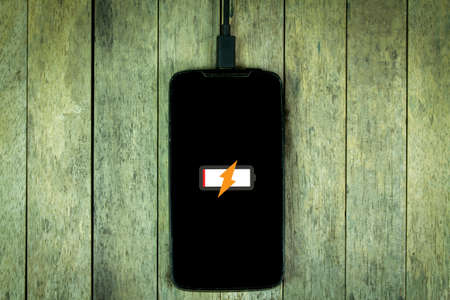 Smart phone is charging on wood background, dark toned with vignette addedの写真素材