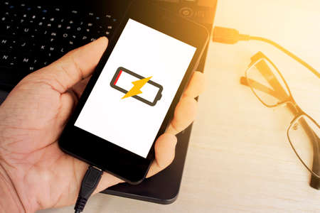 man's hand holding smart phone is charging from laptop sunlight colorの写真素材