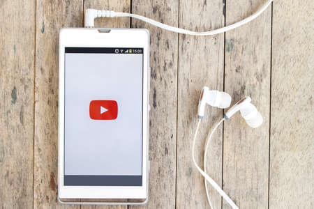 BUNG KAN, THAILAND - MARCH 22, 2016: smart phone display youtube app with earphones on wood backgroundのeditorial素材