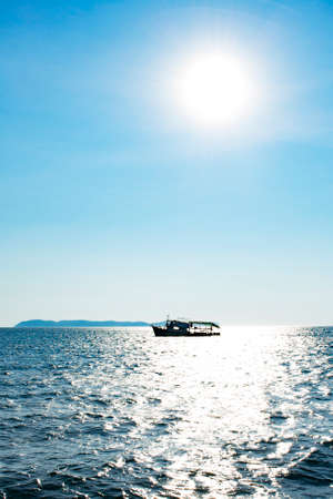 silhouette fishing boat in the ocean with sun and blue sky, back light with vignetteの写真素材