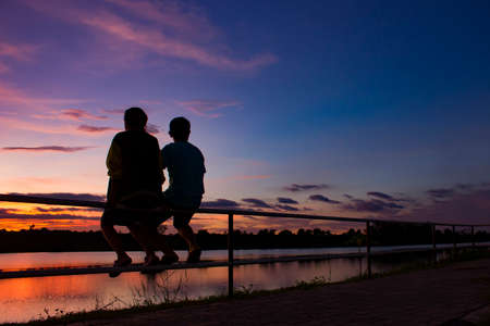 silhouette man and woman couple sitting on the iron bar at sunsetの写真素材