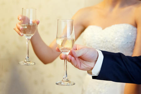 the bride and groom are holding champagne glasses in their hands in the summer near the river close-upの写真素材