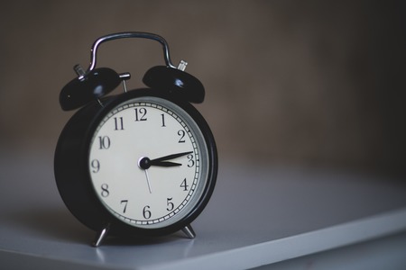 black alarm clock on white table. The concept of the day shift of the beginning and the end of workの写真素材