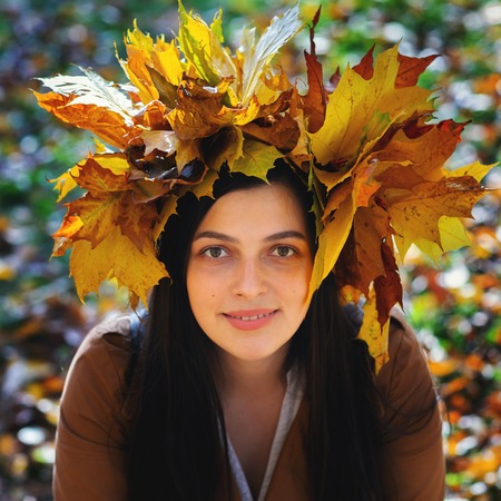 Outdoors lifestyle close up portrait of charming young woman wearing a wreath of autumn leaves. walking on the autumn park. Wreath of maple leavesの写真素材