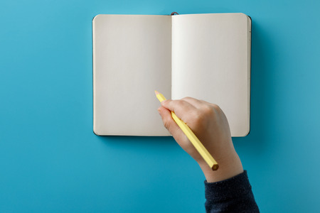 Child hands holding a large spiral notepad with mockup for your design. Blue background.