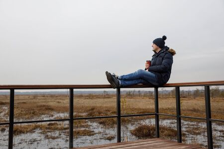 A guy in nature sits and looks at the horizon and drinks coffee.の写真素材