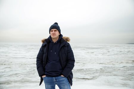portrait of a man on a lake in winter. The guy in the hat and jacket against the ice