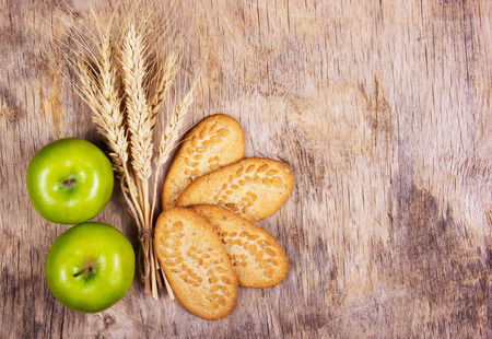Useful snack. Grain organic cookies and juicy green apples. Wheat ears on an old wooden background. Copy spaceの写真素材