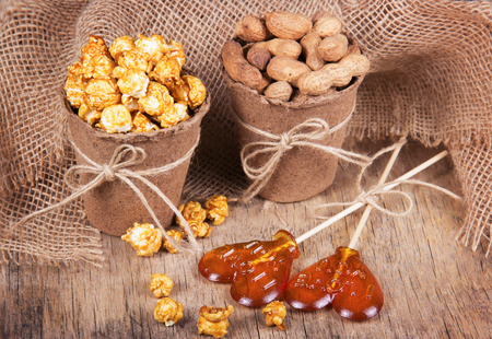 Paper bucket of caramel popcorn, roasted peanuts in shell, and lollipops. Set meal for a movie. Not healthy food and snacksの写真素材