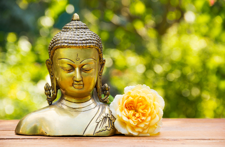 Chinese buddha sculpture and yellow rose flower on natural blur green background. Spa concept. Calmness and tranquility. Copy space.の写真素材