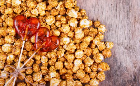 Two lollipop in heart shape and caramel popcorn on wooden background. Copy spaceの写真素材