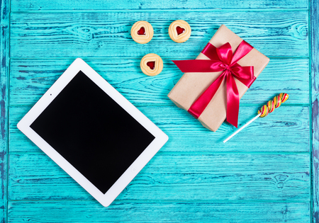 Blue old desk with tablet computer, gift box with bow, cookies with marmalade, lollipop. Top view. Flat layの写真素材