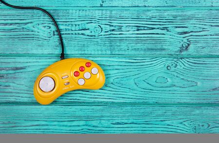 Yellow retro joystick on a turquoise background. Video game console GamePad on a old blue wooden background table. Top viewの写真素材