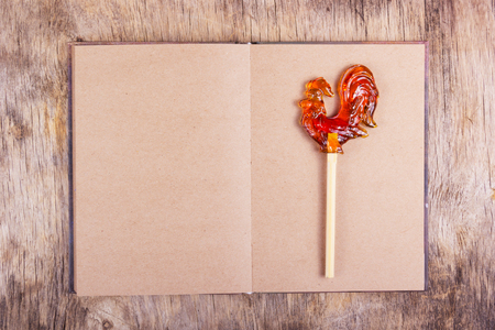 Open book with blank pages and a rooster on a stick. Lollipop on a stick in the form of a rooster on an empty sheet. Copy space.の写真素材