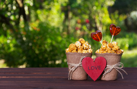 Sweet golden popcorn and lollipops. Set for lovers. Popokorn in a paper bucket and candy hearts. Romantic conceptの写真素材