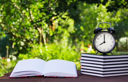 A stack of textbooks and a clock on a wooden table. Homework and education.