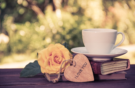A cup of summer tea on a stack of books and a fragrant yellow rose. Romantic concept. Vintage tintingの写真素材