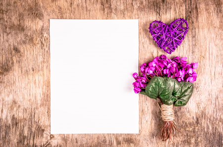 The first spring flowers and wicker heart on a wooden board. Flowers and blank sheet of paper. Romantic concept.の写真素材