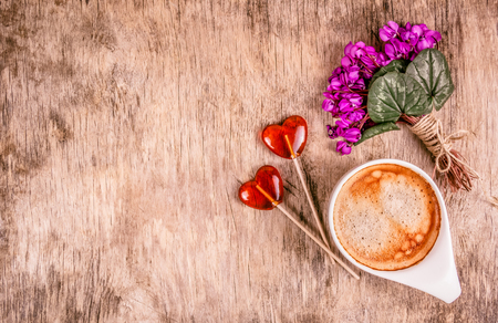 Heart shaped lollipop. Cup of coffee, spring flowers and lollipops. Delicate violets on wooden board. Copy spaceの写真素材