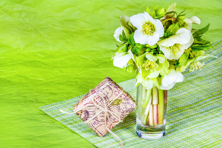 Bouquet of spring flowers and gift box on green paper background. Bouquet of hellebells in glass.の写真素材