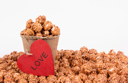 Chocolate caramel popcorn in paper bucket on white background. Popcorn and red heart. Romantic concept. St. Valentine's Day.の写真素材