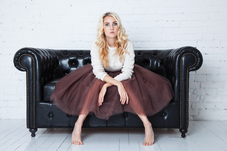 Elegant young woman in lush skirt sits on the couch. Concept fatigueの写真素材
