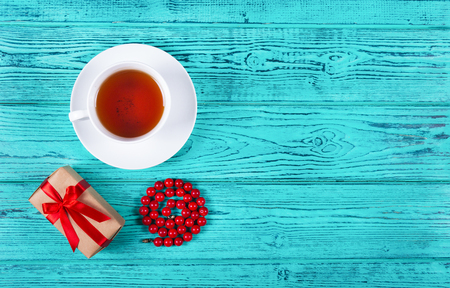 Romantic gift with red bow and cup of tea on wooden background. Gift for woman's day. White cup of tea. Copy space. Top viewの写真素材