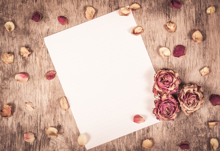 Empty sheet of paper, dried roses and wooden background. Empty letter. Note on wooden background.の写真素材