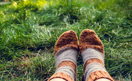 Feet in warm woolen socks. Knitted wool socks. Feet in socks on the background of green grass. Autumn concept, travelの写真素材