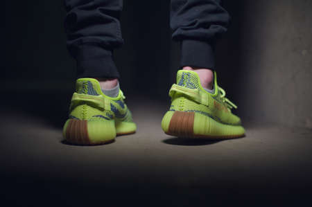 A man wearing Adidas Yeezy Boost 350 v2 Sply semi frozen yellow sport shoes shot on dark grey background. Close up view of sneakers. Krasnoyarsk, Russia - December 26, 2017のeditorial素材