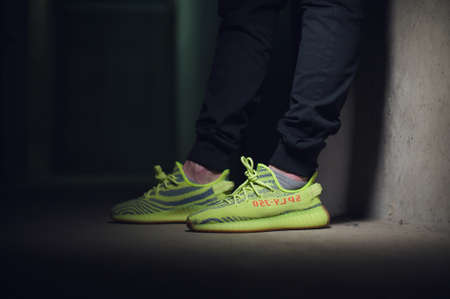A man wearing Adidas Yeezy Boost 350 v2 Sply semi frozen yellow sport shoes shot on dark grey background. Close up view of sneakers. Krasnoyarsk, Russia - December 26, 2017のeditorial素材