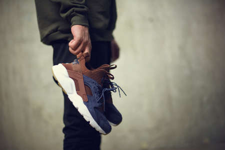 Young man with brown Nike Air Huarache sport shoes in hand shot on grey background. Nike sneakers,...