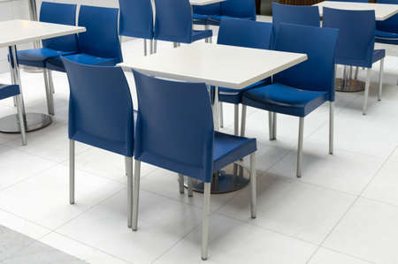 Interior of public dining area with blue plastic chairs and white tables. Empty table on food court in business shopping center, modern interior design.の写真素材