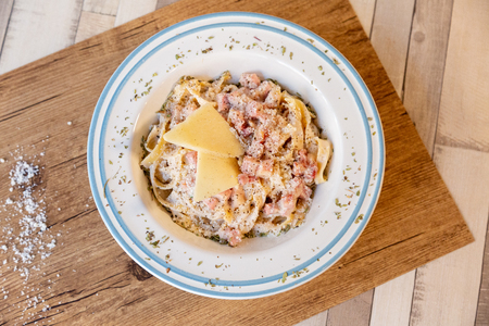 A top view of a carbonara spaghetti plate on a wooden table with cheese, bacon and pepperの写真素材