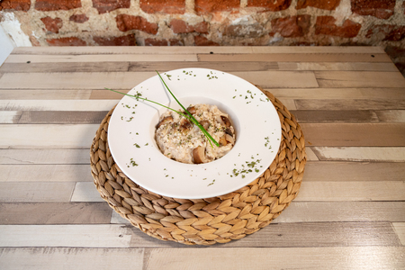 A plate of mushroom risotto in a wooden table with a white plate garnish with oregano and a brick wall.の写真素材