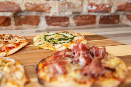 pizzas on a wooden board with focus in a pesto pizza in a wooden table with a brick wallの写真素材