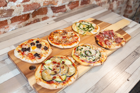 Aerial view of six different pizzas on a wooden board on a wooden table with a brick wallの写真素材