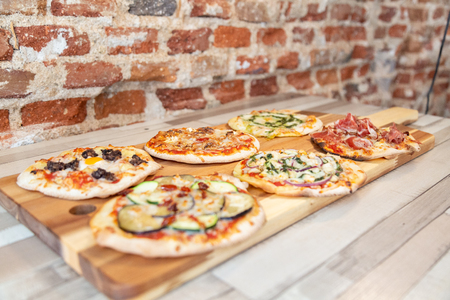 Side view of six different pizzas on a wooden board on a wooden table with a brick wallの写真素材