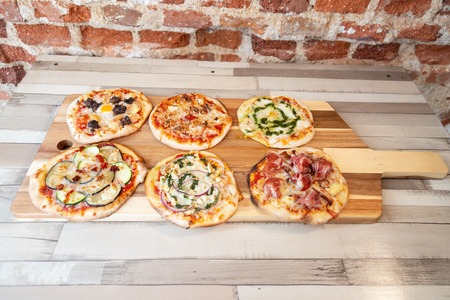 Aerial view of six different pizzas on a wooden board on a wooden table with a brick wallの写真素材