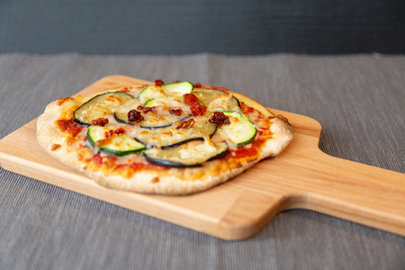 pizza with zucchini, eggplant and dry tomatoes with gratin mozzarella cheese. On a wooden board and gray tableclothの写真素材