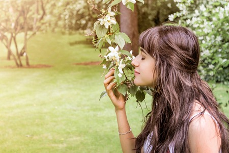 pretty brunette girl with long hair smelling a flower on the natureの写真素材